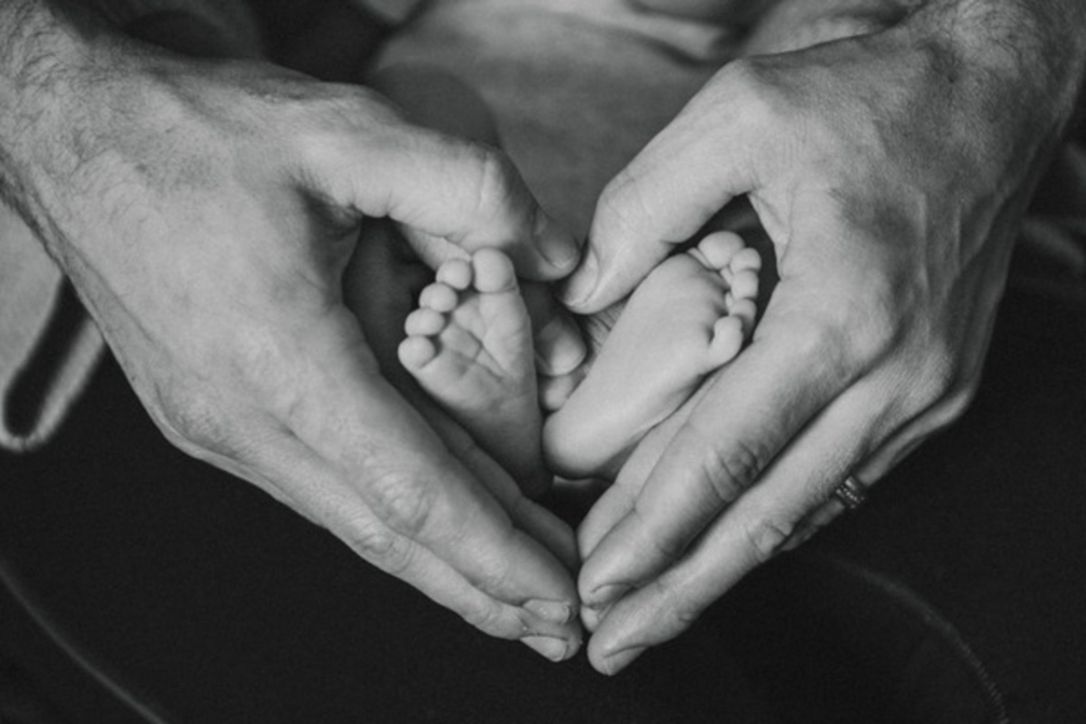Les pieds de bébé dans les mains des parents qui forment un coeur